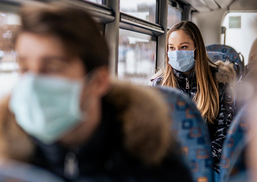 Woman wearing face mask because of COVID-19. She is sitting on a bus. She is looking outside the window.