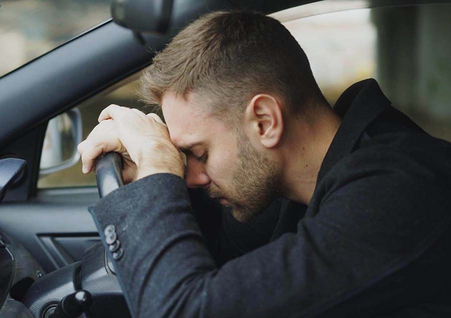 Young man sitting in car with his head on the steering wheel